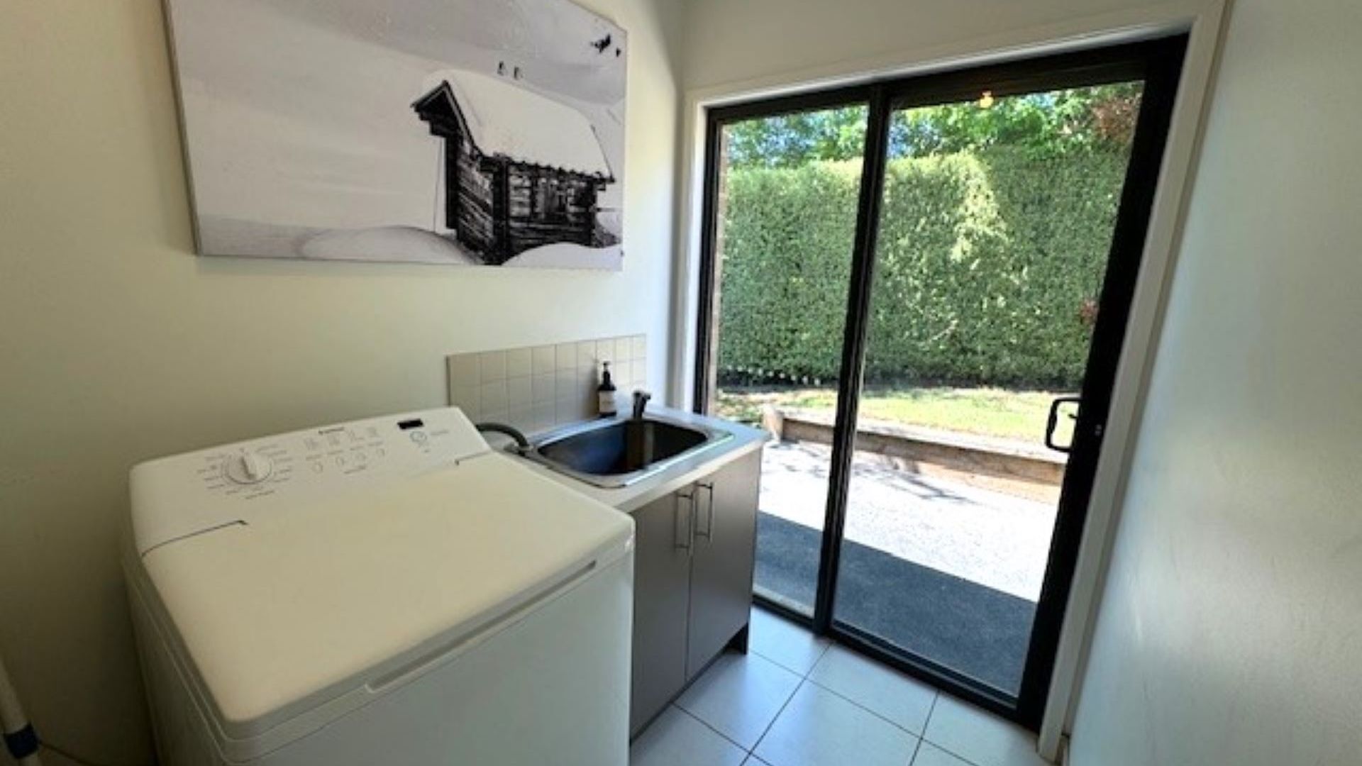 Une cuisine compacte équipée d’un lave-linge, d’un évier et d’une porte-fenêtre coulissante donnant sur une terrasse.