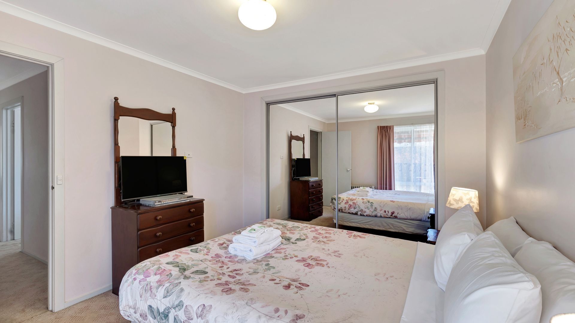 A bedroom with a bed, a dresser, a television, and a mirror.