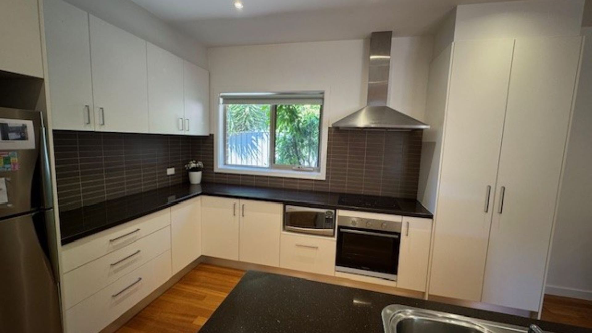 A modern kitchen with white cabinets, a black countertop, a window, and a stainless steel range hood.