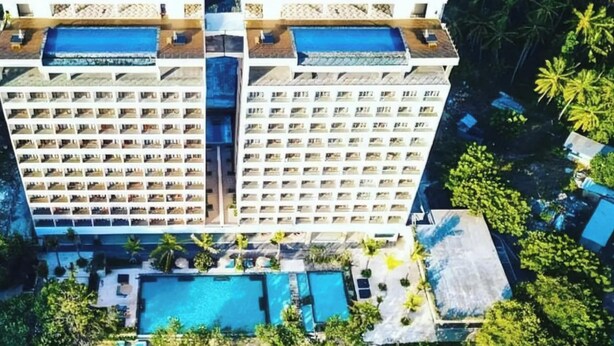 Un hotel de gran altura con varios balcones, zona de piscina y vista a la playa.