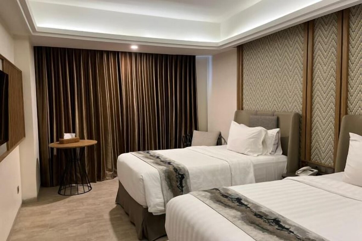 Une chambre d’hôtel avec deux lits, une petite table ronde et un rideau servant de décor.