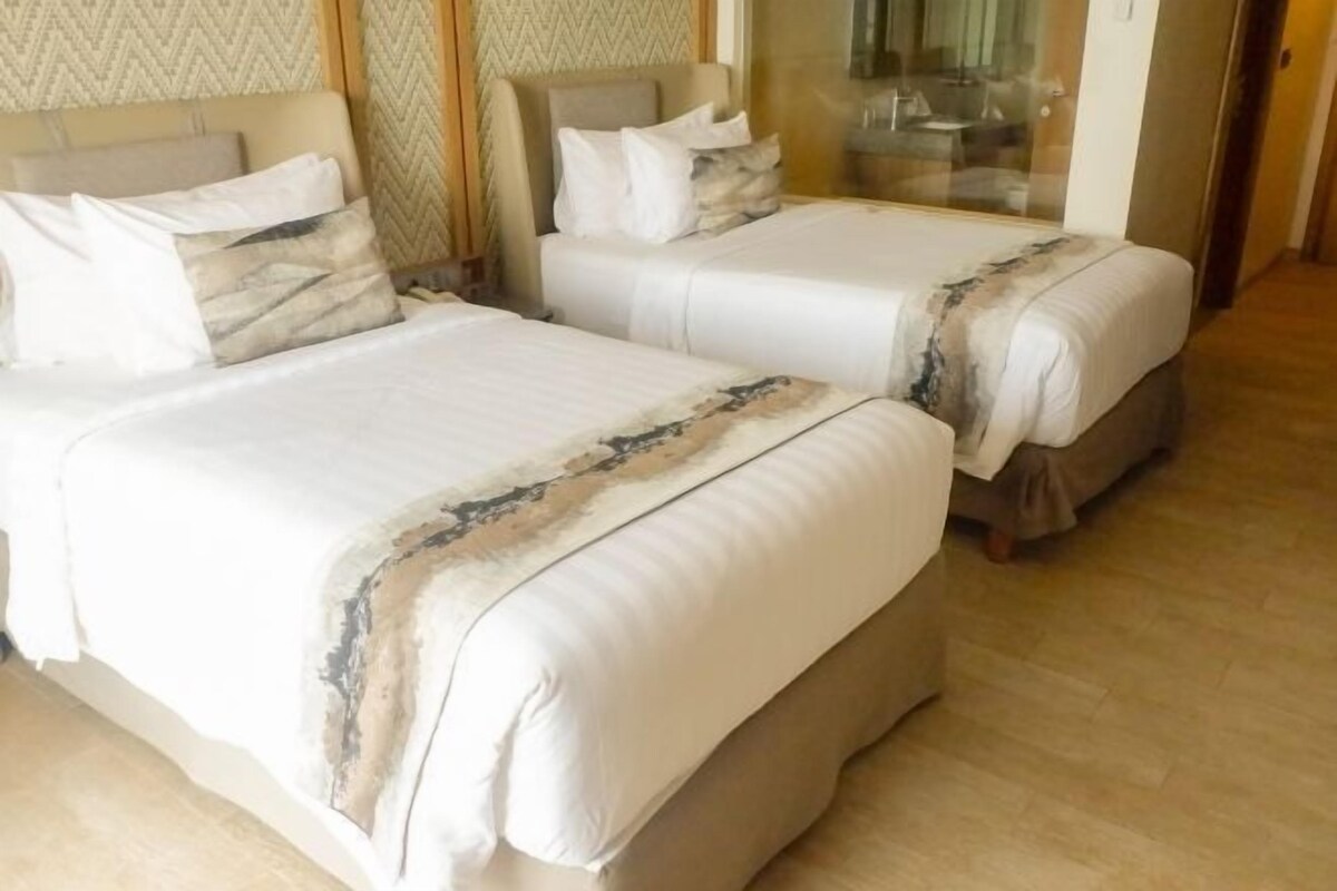 Habitación de hotel con dos camas, cada una con cabecero y almohadas.