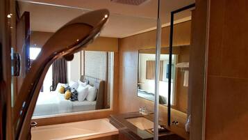 Une chambre d’hôtel moderne avec un grand lit, une douche à parois de verre et un grand miroir.