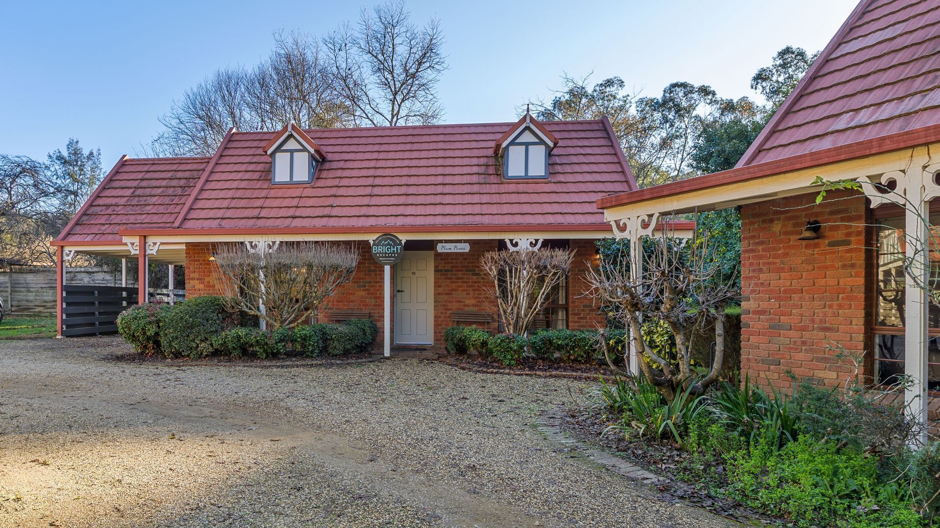 A two-story brick house with a red tiled roof, a covered porch, and a gravel driveway.