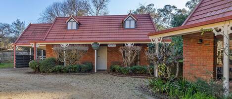 A two-story brick house with a red tiled roof, a covered porch, and a gravel driveway.