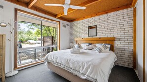 A bedroom with a large bed, a wooden headboard, a ceiling fan, and a brick wall. - Kalamunda 6 - On the Rail Trail (BRIGHT)