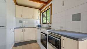 A compact kitchen with white cabinets, a built-in oven, a microwave, and a window providing natural light. - Kalamunda 6 - On the Rail Trail (BRIGHT)