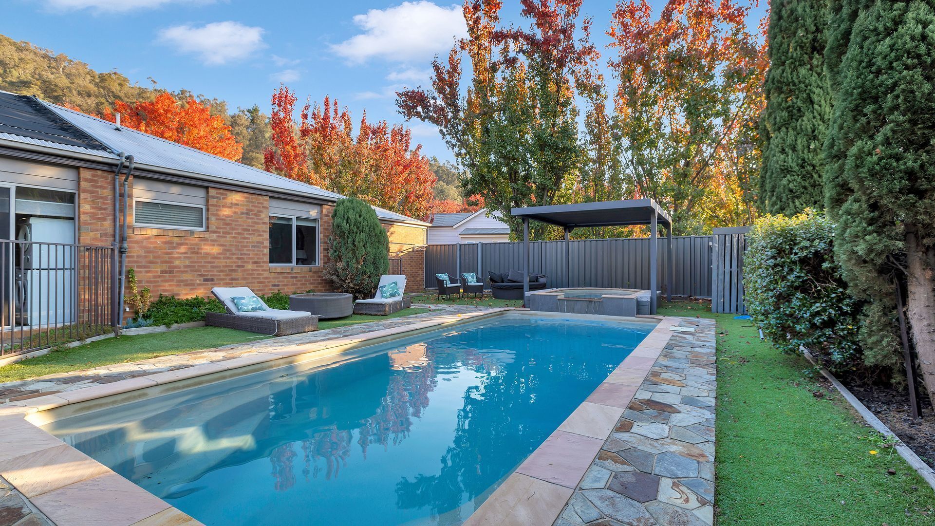 A backyard with a swimming pool, a patio area with seating, and a covered outdoor space.