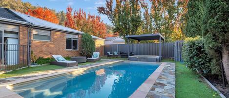 A backyard with a swimming pool, a patio area with seating, and a covered outdoor space.