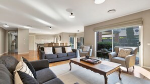 A spacious living area with a dark grey sofa set, a wooden coffee table, and a dining area in the background.