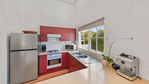 Una cocina moderna con un refrigerador de acero inoxidable, armarios rojos, un microondas, una estufa y un lavamanos.