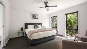 A bedroom with a bed, a bedside table, a chair, a ceiling fan, and a window with a view of greenery. - 2 Minutes By Bike - On the Rail Trail (BRIGHT)