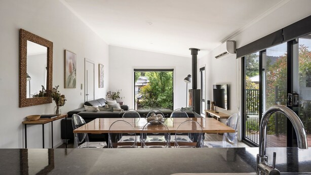 A modern dining area with a wooden table and chairs, a sofa, and a large mirror on the wall. - 2 Minutes By Bike - On the Rail Trail (BRIGHT)