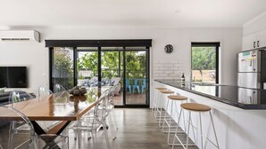 A modern kitchen with a long counter, bar stools, and a dining area with a glass table and chairs. - 2 Minutes By Bike - On the Rail Trail (BRIGHT)