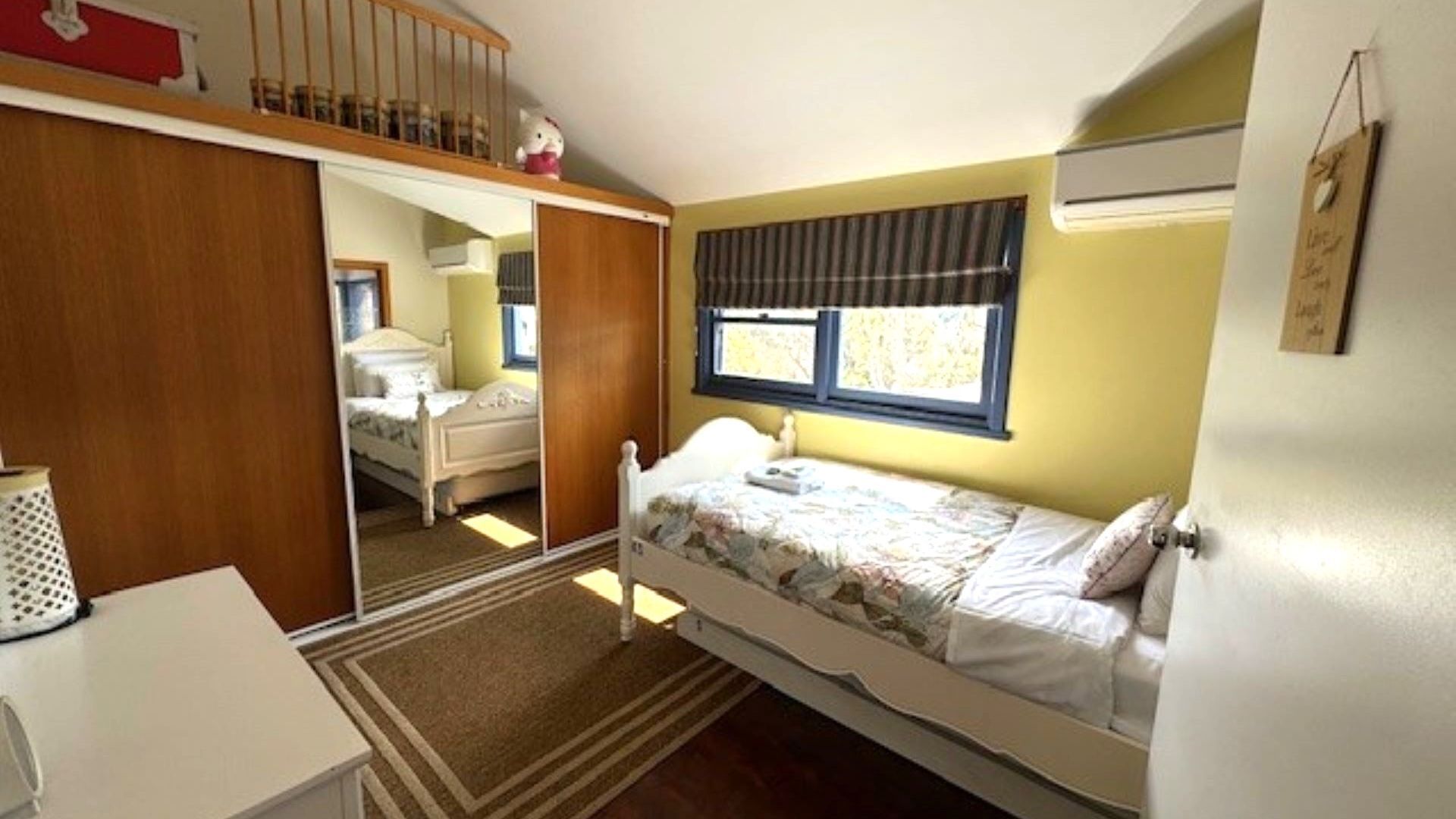 Une chambre à coucher de taille réduite, comprenant un lit simple, un petit bureau et une armoire.