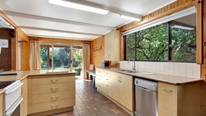 Eine moderne Küche mit Holzausstattung, einem eingebauten Geschirrspüler und einem großen Fenster mit Blick ins Grüne.