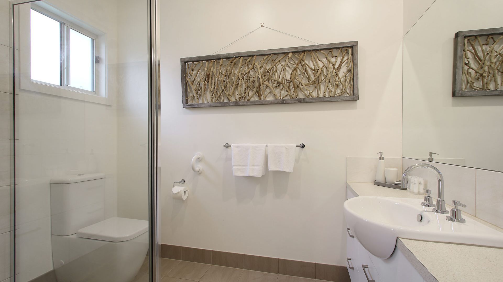 A modern bathroom with a glass shower enclosure, a white sink with a mirror, and a wall-mounted towel rack.