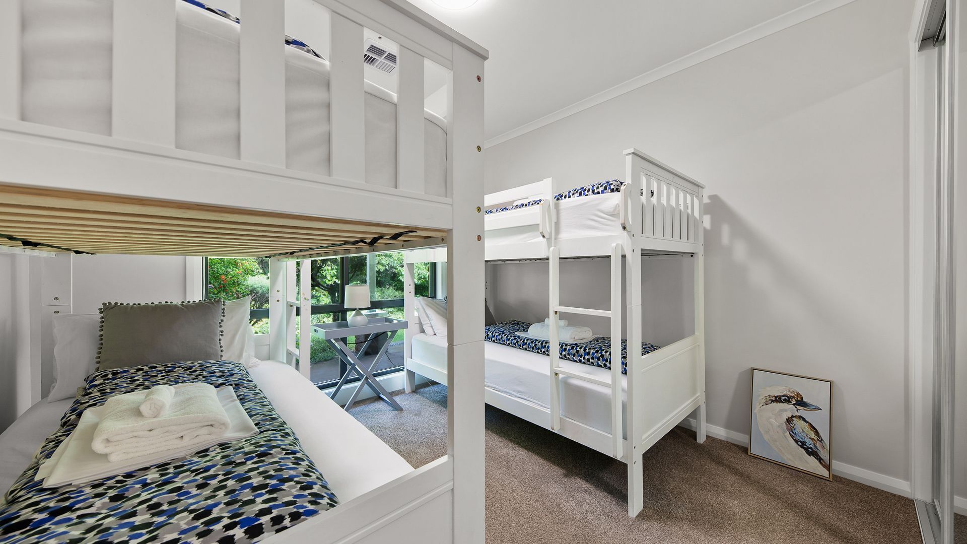 A room with two bunk beds, a small table with a chair, and a framed picture on the wall.