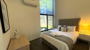 Une chambre à coucher bien aménagée, avec un grand lit, une table de chevet, une commode et une fenêtre donnant sur des arbres.