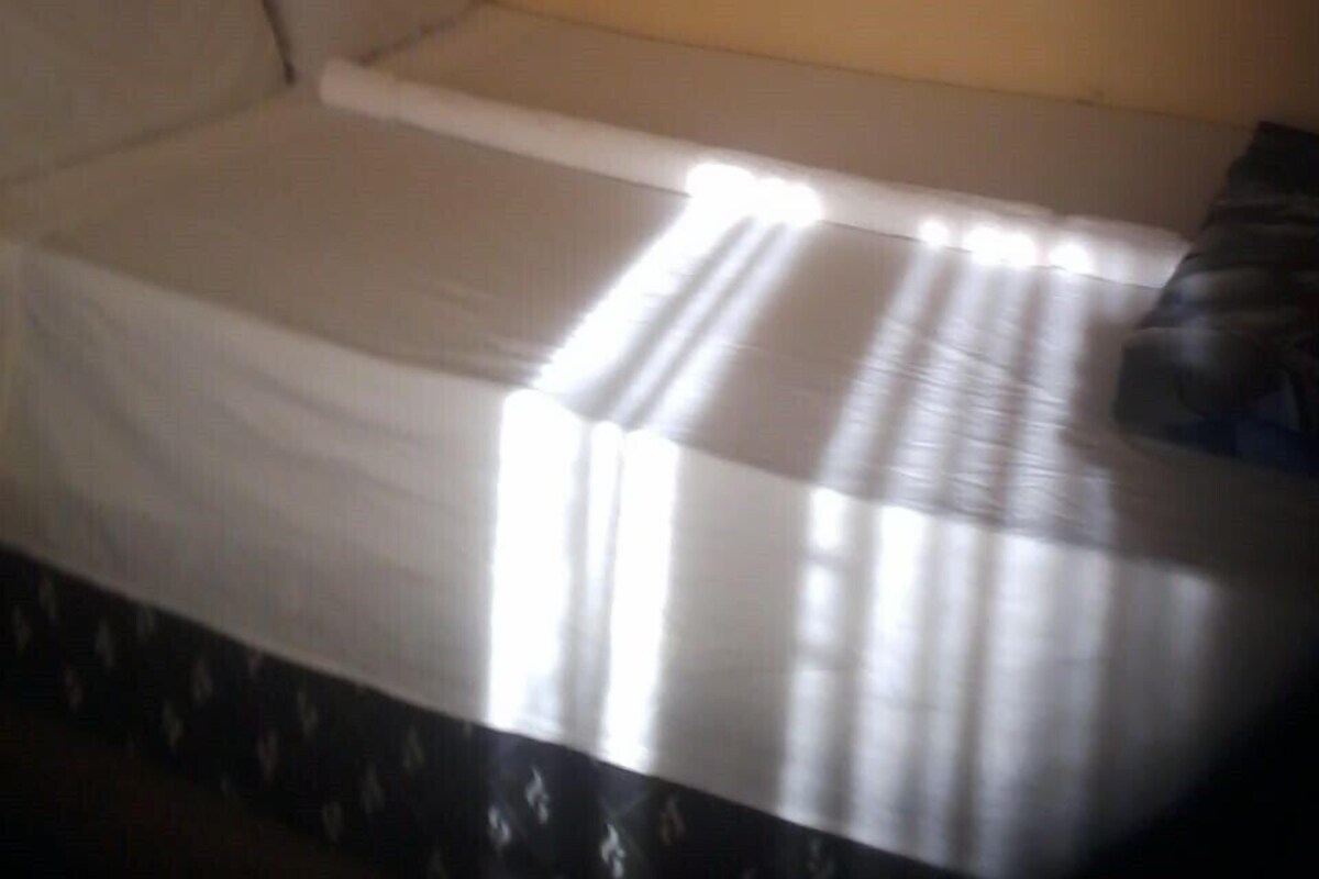 Una cama individual con un colchón blanco y cabecera frente a una pared lisa.