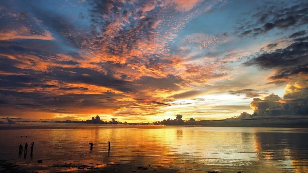 A sunset over a calm body of water with a distant shoreline and a few structures.