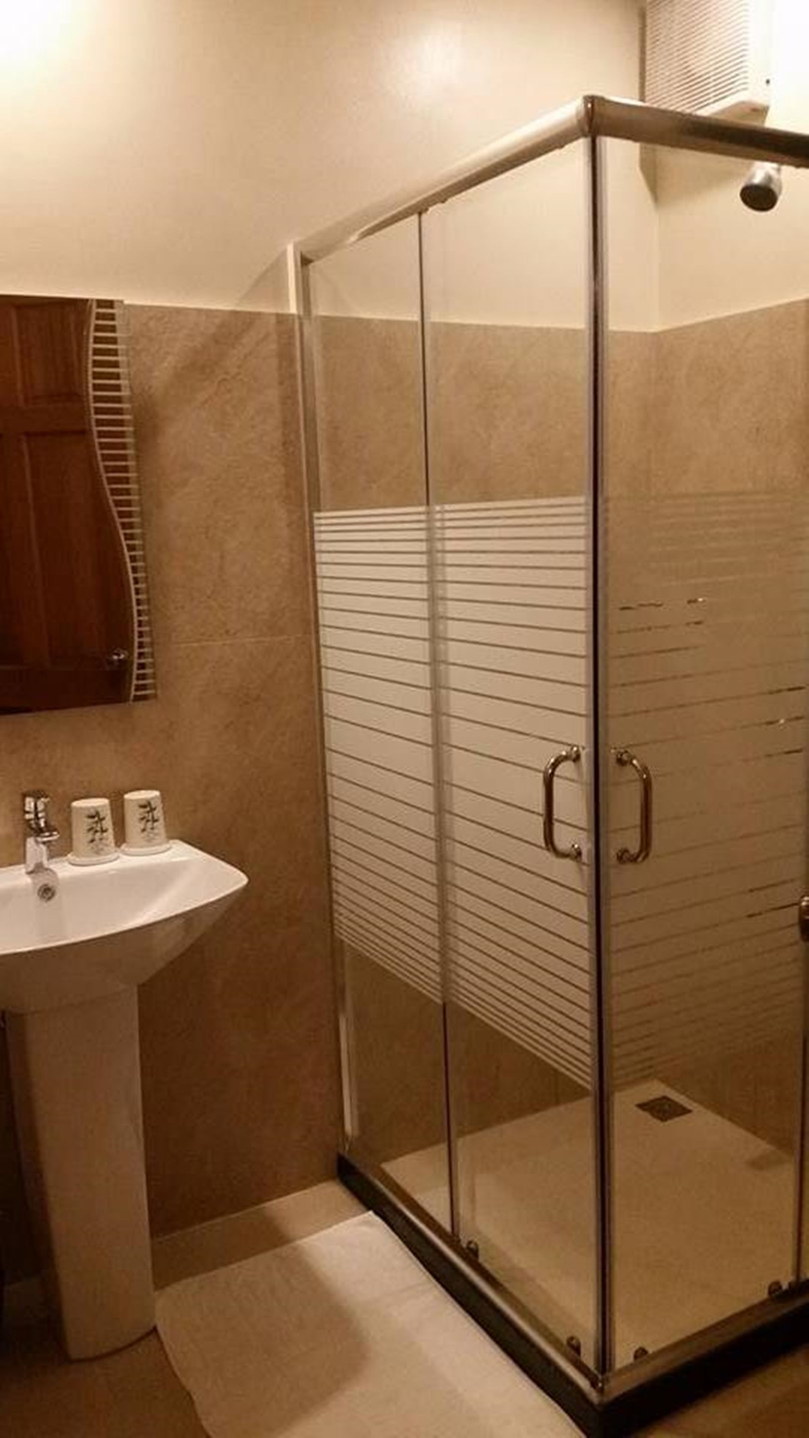 A bathroom with a glass-enclosed shower, a white sink, and a wooden cabinet.
