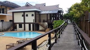 A hotel with a swimming pool, wooden deck, and a staircase leading to the upper floors. - Infinity Sands Resort (San Juan)