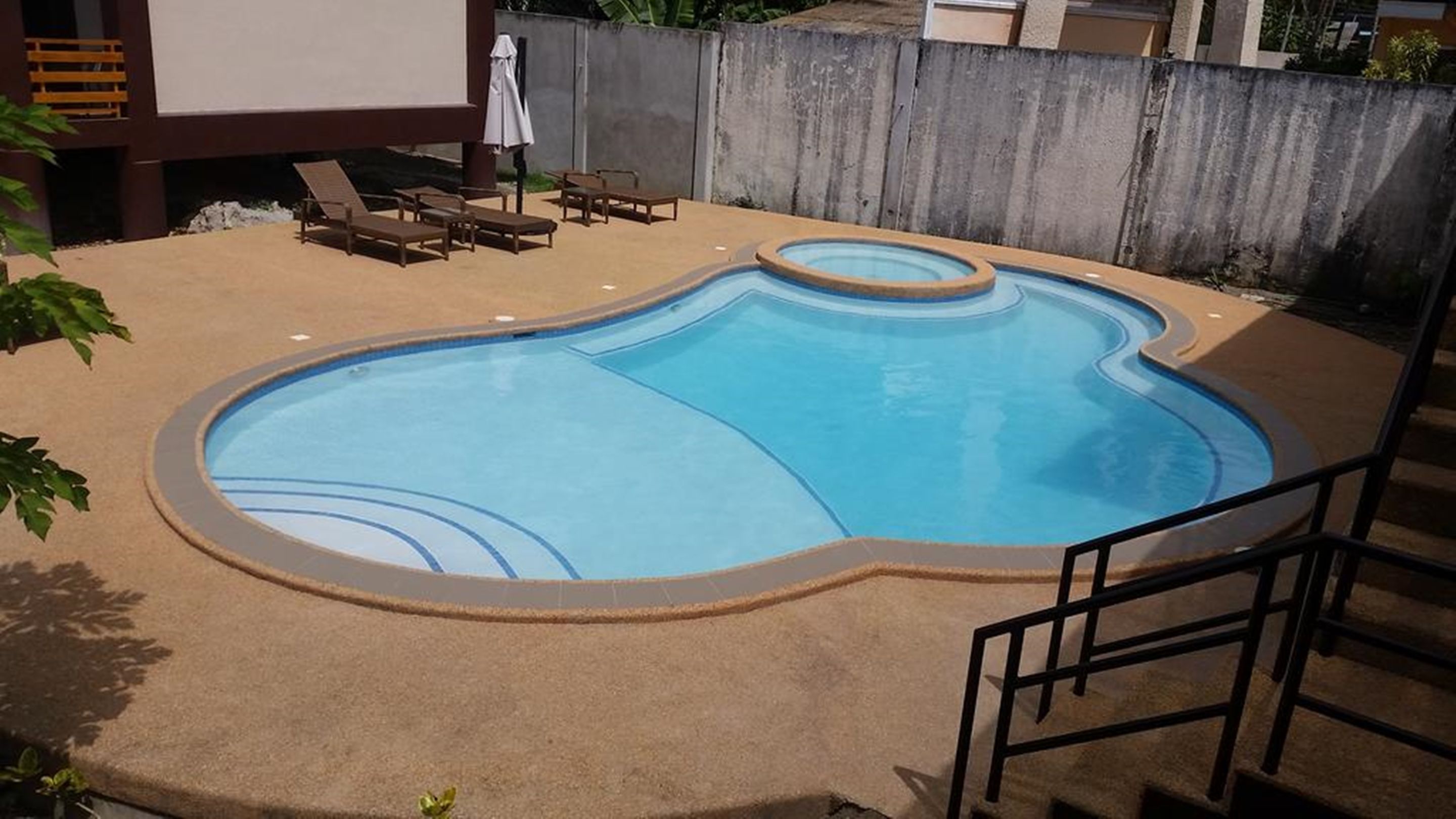 A swimming pool with a unique shape, surrounded by a concrete deck and a wooden fence.