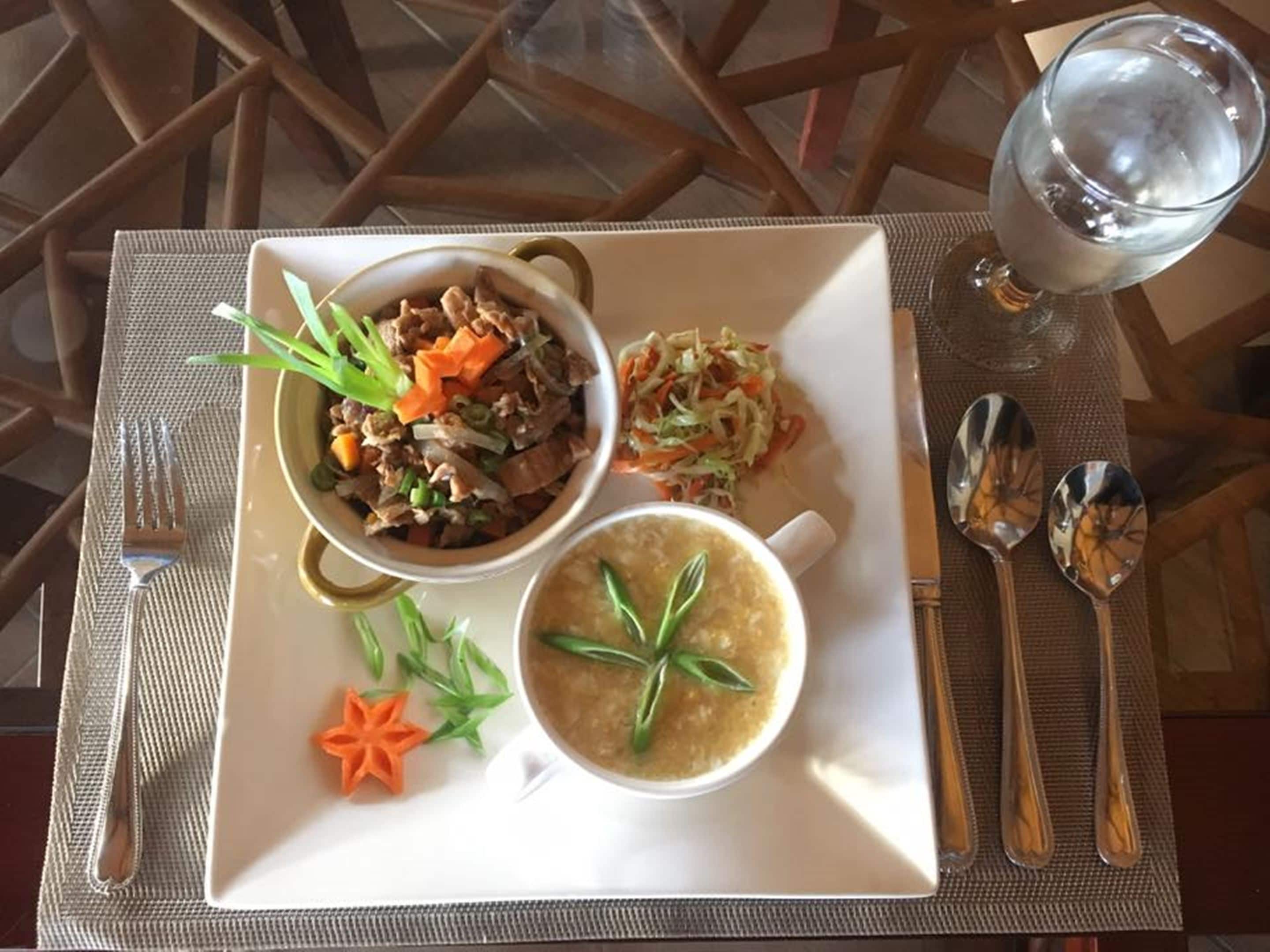 En tallerken med suppe, kødret og salat, samt bestik og et glas vand på et bord.