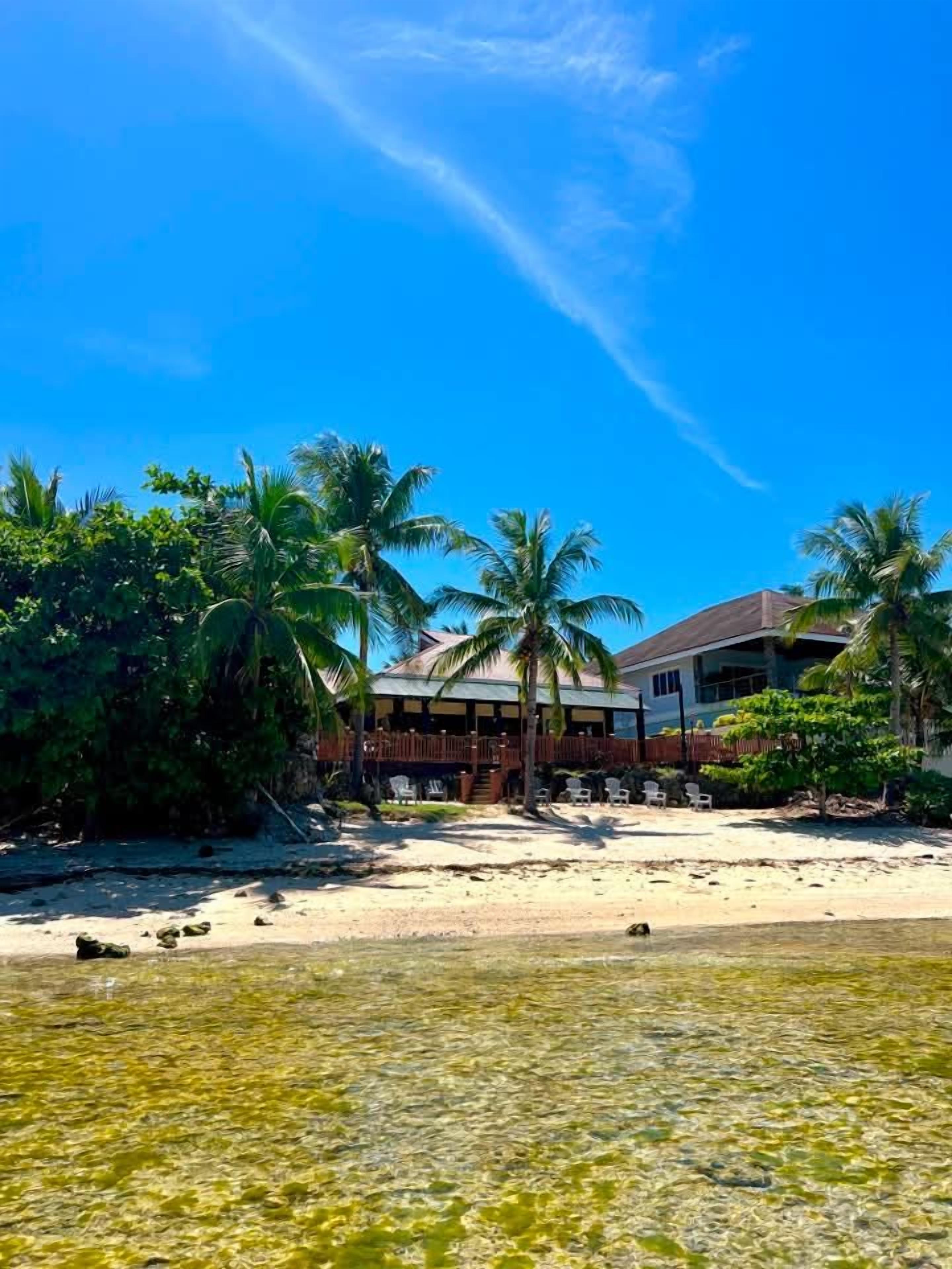 A beachfront property with a wooden deck, palm trees, and a clear blue sky.
