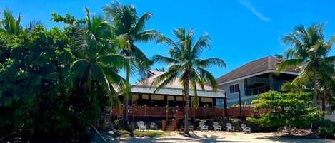 A beachfront property with a wooden deck, palm trees, and a clear blue sky.