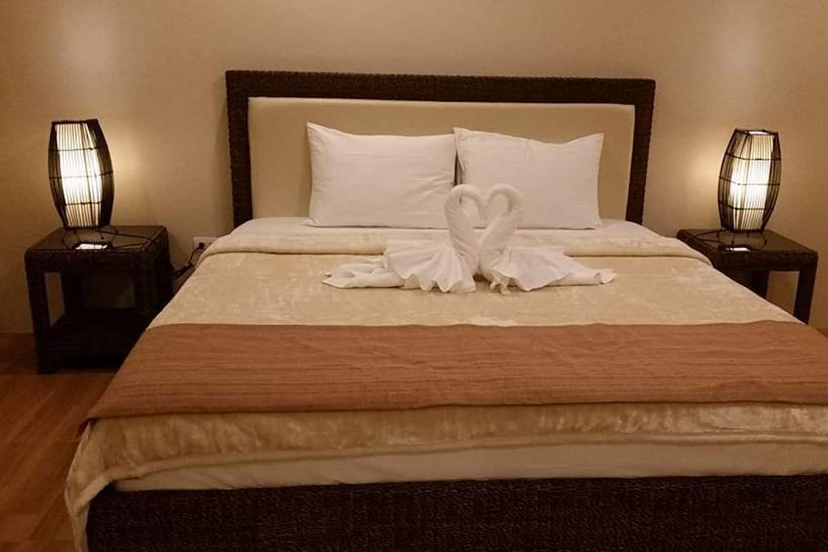 A neatly made bed with a brown bedspread and white pillows, flanked by two bedside tables with lamps.