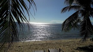 A beach with two wooden chairs facing the ocean, palm trees, and a clear sky. - Infinity Sands Resort (San Juan)