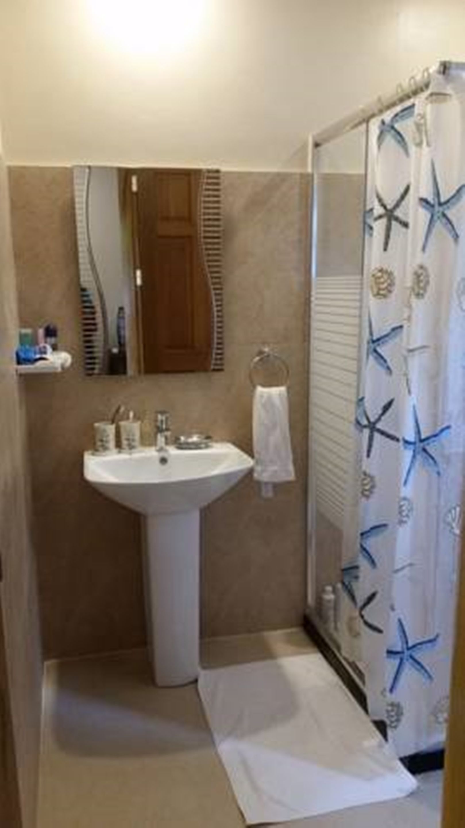 A bathroom with a pedestal sink, a mirror, a towel rack, and a shower curtain with starfish designs.