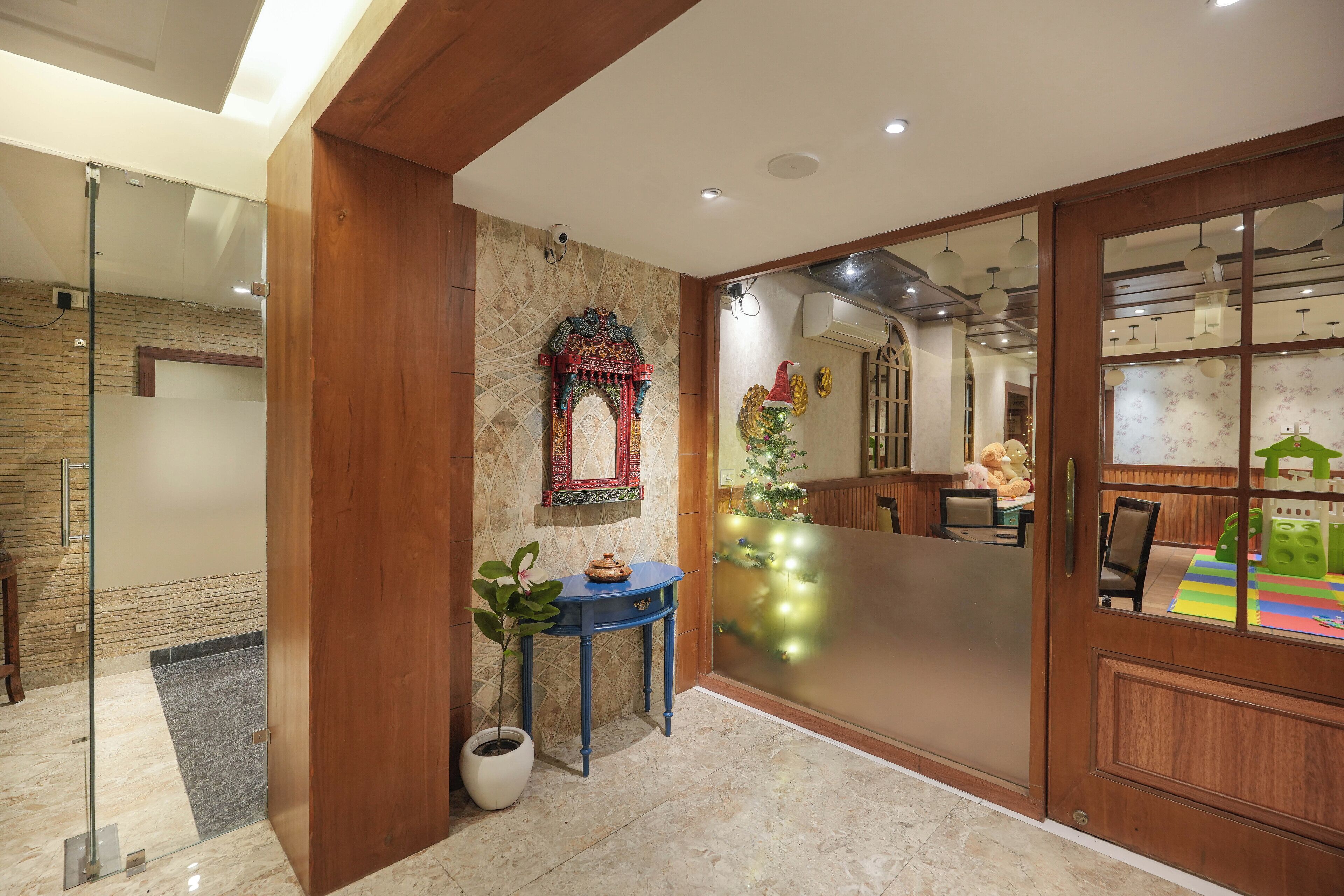Un interior moderno con una puerta de madera, un separador de vidrio, un arco decorativo y una mesita con una planta.