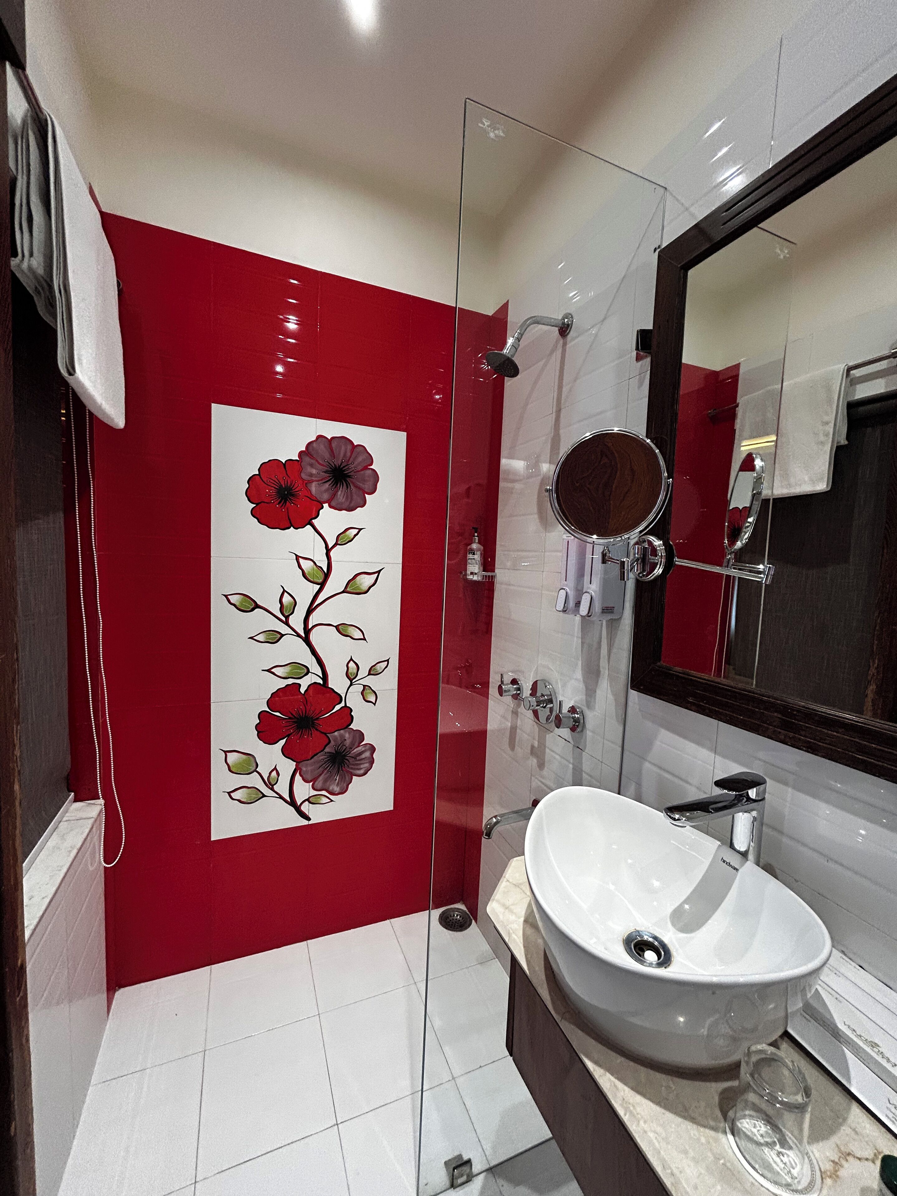 Une salle de bain moderne avec un lavabo blanc, une cabine de douche en verre et un motif floral rouge sur le mur.