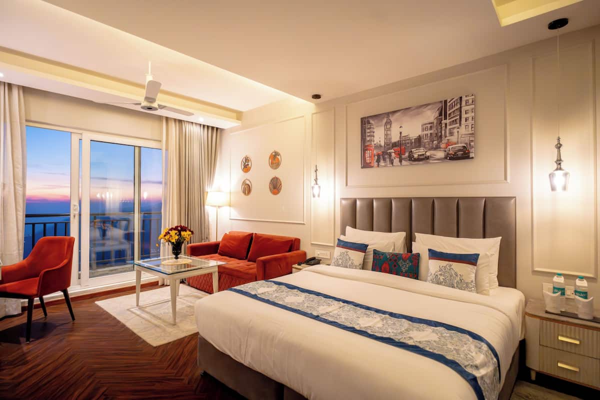 A hotel room with a large bed, a sofa, a table, and a balcony with a view.