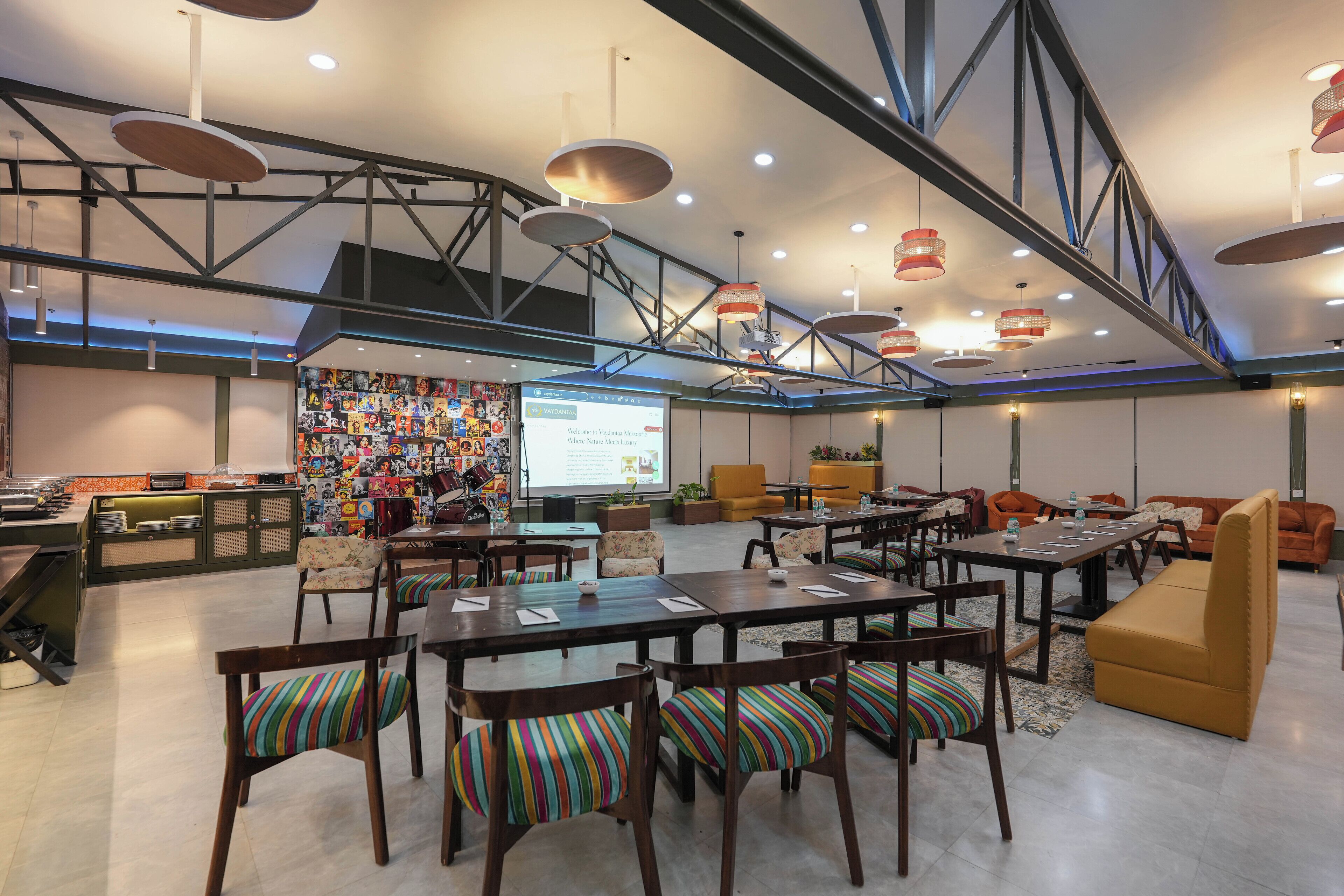 Un'ampia area lounge con varie opzioni di seduta, tra cui tavoli e divani, e un grande schermo che mostra una presentazione.