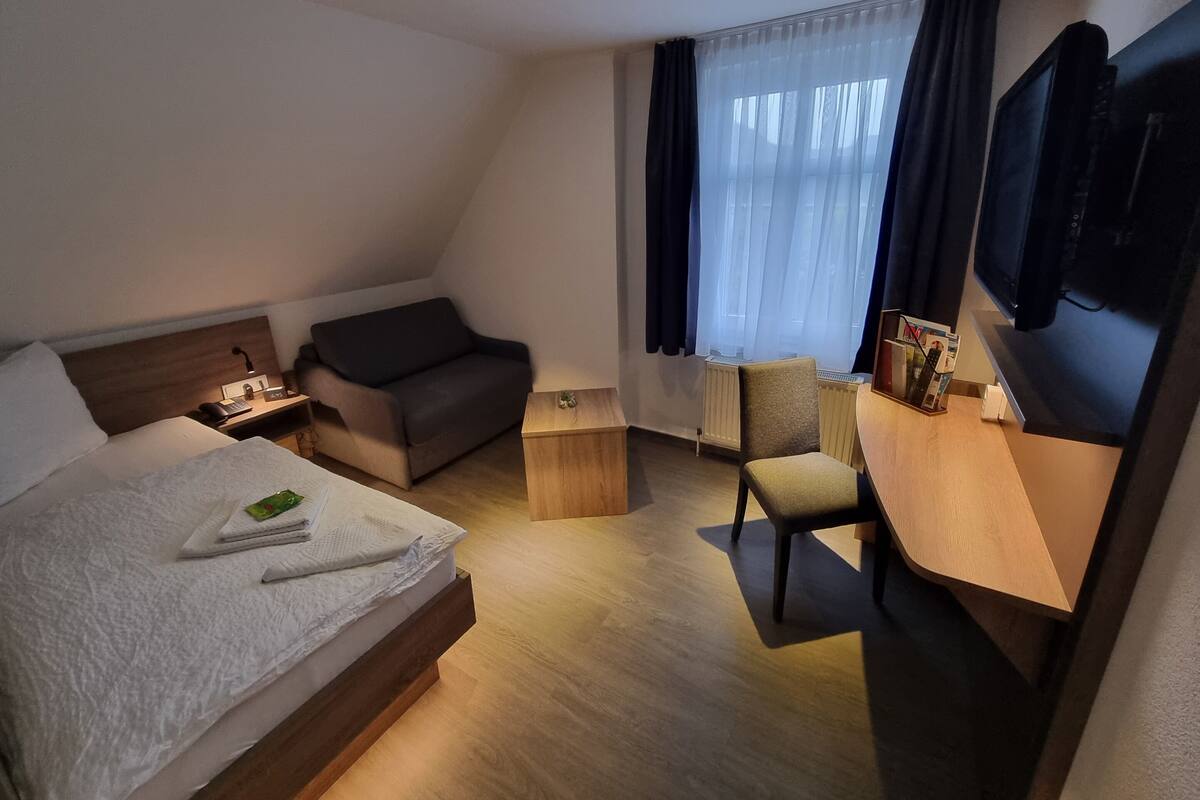 Een hotelkamer met een bed, een bank, een bureau met stoel, een televisie en een raam met gordijnen.
