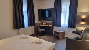 A hotel room with a large bed, a desk, a chair, a sofa, and a TV.