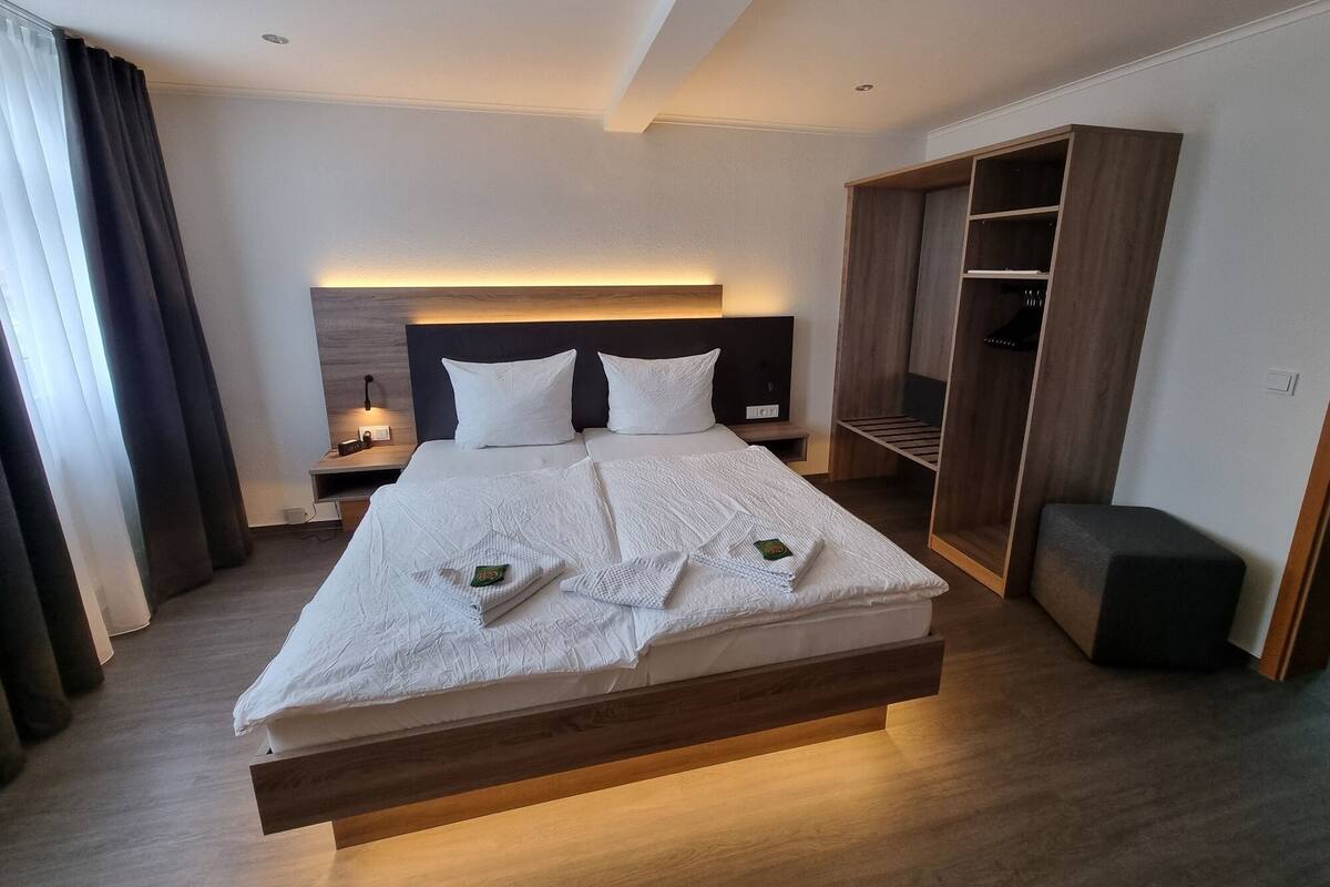Een moderne hotelkamer met een groot bed, een nachtkastje met een lamp, een kledingkast en een klein bankje.