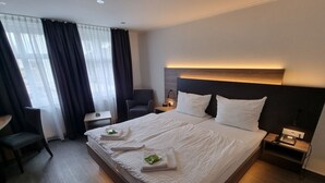 A hotel room with a large bed, a desk, a chair, and a nightstand with a phone.