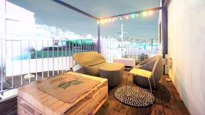 A balcony with wicker furniture, a table with a placemat, and string lights. - Seoul Cube Ewha - Hostel (Seoul)