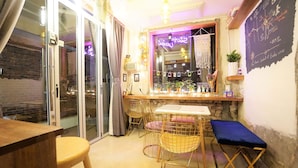 A cozy bar area with a wooden counter, two metal chairs, a bench, and a chalkboard menu. - Seoul Cube Ewha - Hostel (Seoul)
