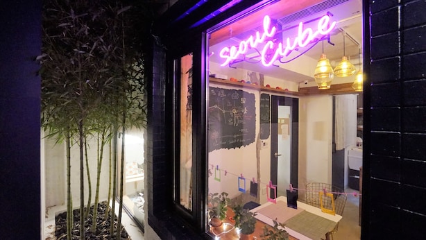 A restaurant with a neon sign reading "Seoul Cafe," a window display with plants, and a visible interior with hanging lights and a counter. - Seoul Cube Ewha - Hostel (Seoul)