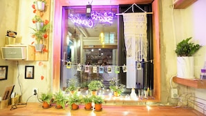 A cozy interior with a wooden counter, potted plants, a neon sign, and a macrame wall hanging. - Seoul Cube Ewha - Hostel (Seoul)
