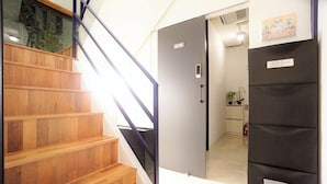 A staircase with wooden steps and a metal handrail leading to a room with a black refrigerator and a small kitchen area. - Seoul Cube Ewha - Hostel (Seoul)
