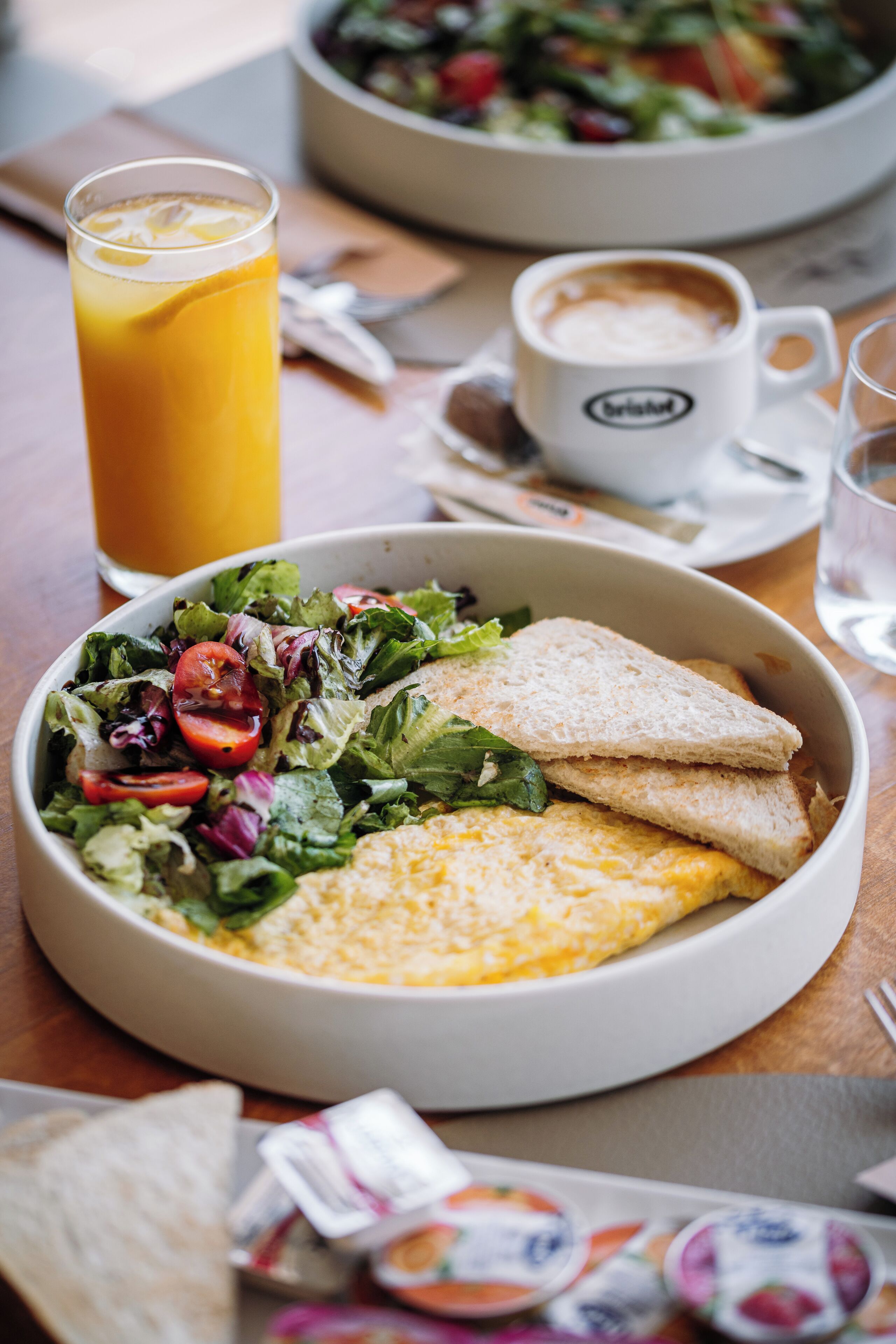 A meal consisting of a salad, omelette, and toast, accompanied by a glass of orange juice and a cup of coffee on a wooden table.