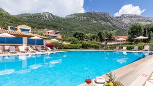 A swimming pool with lounge chairs and umbrellas, surrounded by mountains and greenery. - Akti Barbati Houses by Konnect (Corfu)