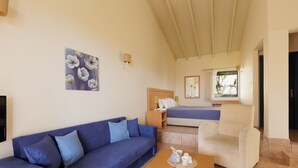 A room with a blue sofa, a wooden coffee table, a bed with a blue bedspread, a white armchair, and a painting on the wall. - Akti Barbati Houses by Konnect (Corfu)